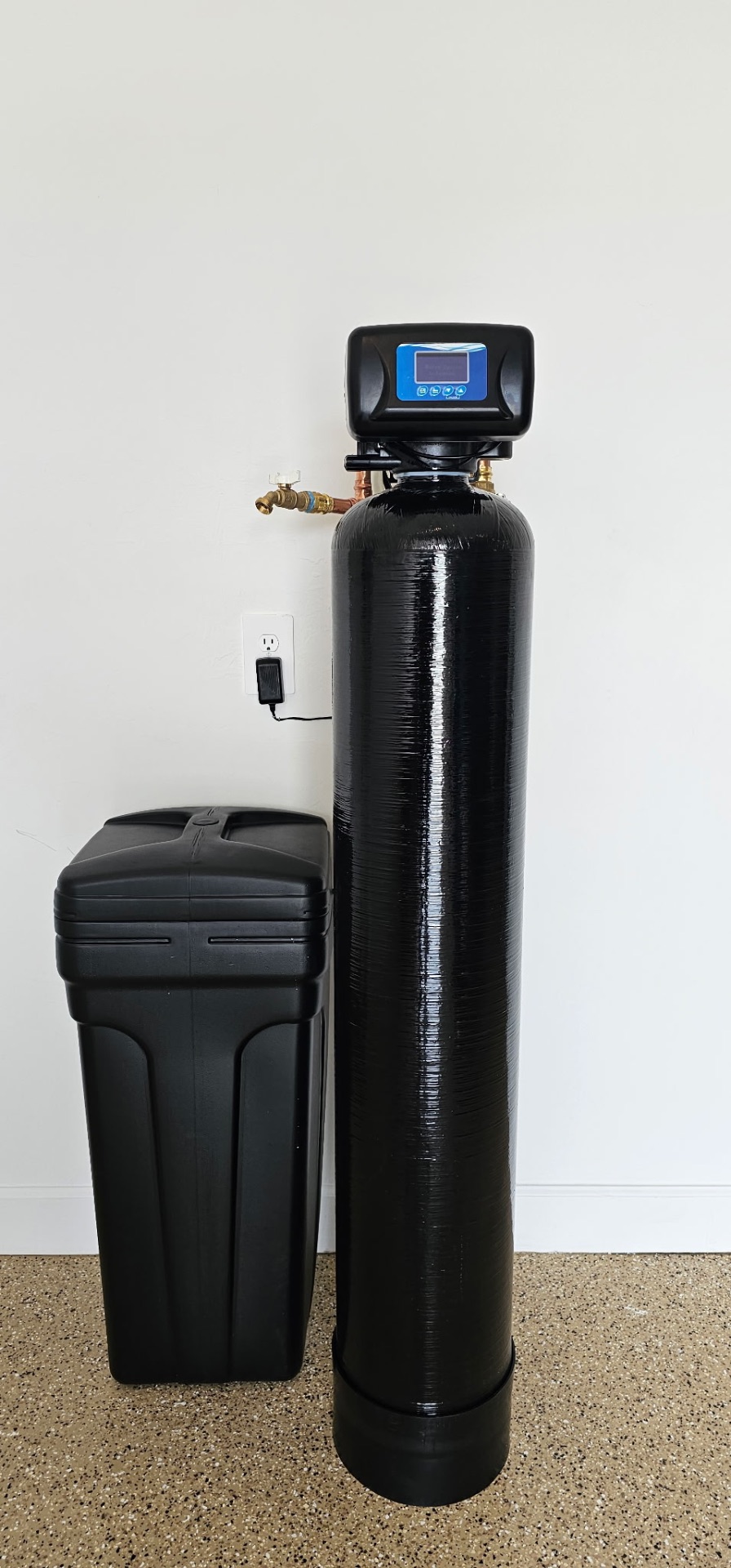 Black whole-home water softener tank with digital valve and brine tank in a Tucson garage